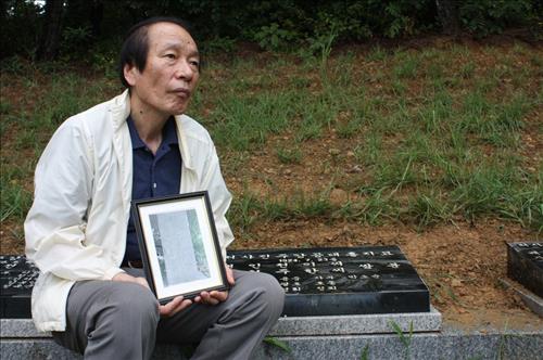 강대흥씨 가묘 앞에 앉아 있는 손자 광호씨. 그가 들고 있는 사진은 일본에 있는 강대흥씨의 묘를 찍은 사진이다.