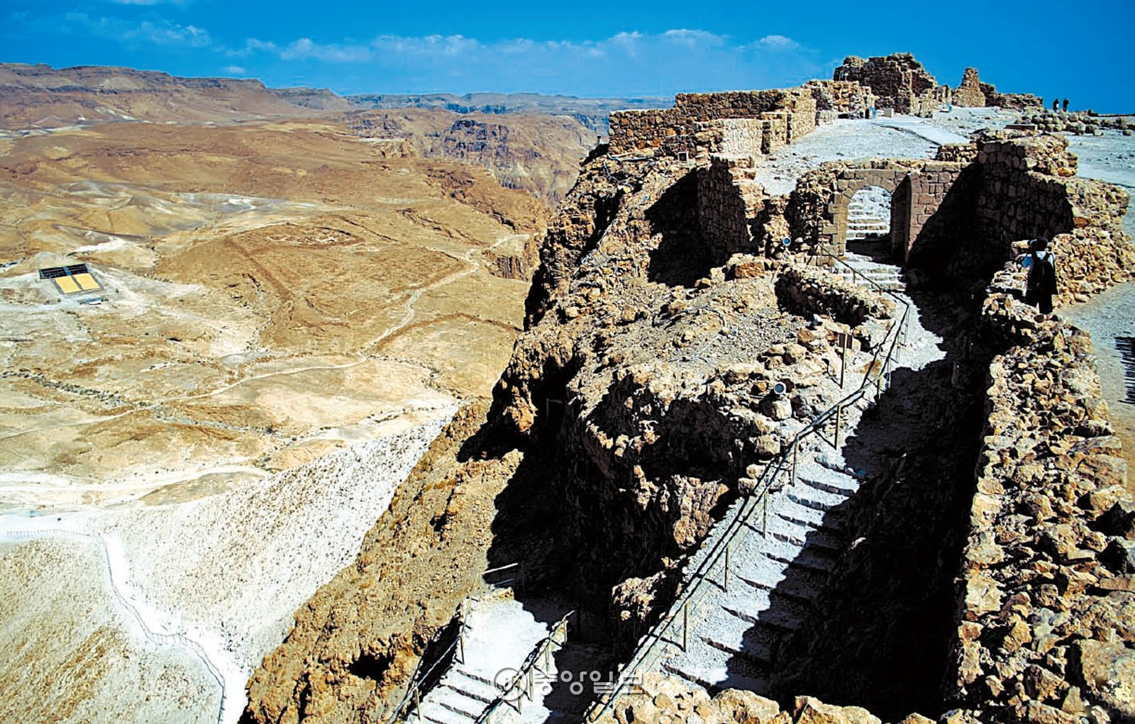 마사다의 절벽에 놓인 가파른 계단. 그 뒤로 로마군이 쌓은 경사로와 그들의 옛 막사터가 보인다.