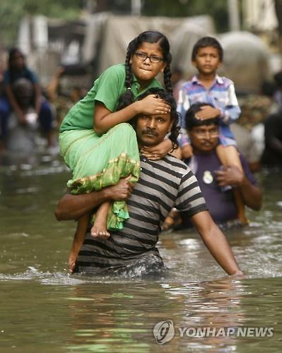 3일(현지시간) 인도 첸나이에서 주민들이 어린이들을 어깨 위에 태운 채 허리까지 찬 물을 헤치고 이동하고 있다.(AP=연합뉴스)