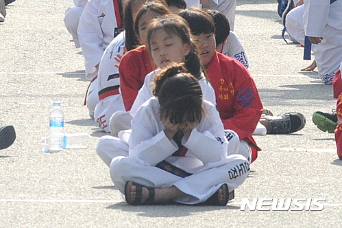 18일 전북도청 앞에서 무주태권도선수권대회 성공을 염원하는 행사가 열린 가운데 퍼포먼스에 참여한 초등학생들이 더위에 지친 모습으로 앉아 있다.