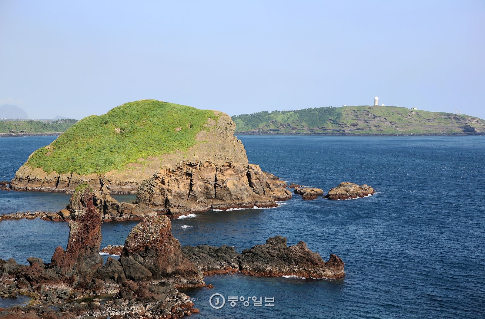 차귀도는 해안을 따라 기암괴석이 솟아 있다. 앞에 보이는 돌기둥이 장군석이고 뒤에 보이는 해안 언덕이 수월봉이다.