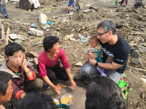 수해지역에서 긴급구호활동을 펼치고 있는 무라트 사힌 유니세프 북한 주재 부대표(오른쪽)가 땅바닥에 쪼그리고 앉아 식사 중인 주민들과 대화를 하고 있다.  유니세프 제공