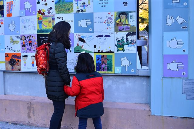 서울농학교 담장에 그려진 그림과 수화를 엄마와 아이가 함께 보고 있다.