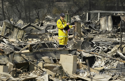 11일(현지시간) 산불 피해가 극심한 미국 캘리포니아 샌타로자 시 화재 현장에서 잿더미로 변한 이동주택 내부를 살피는 소방당국 요원[AP=연합뉴스]