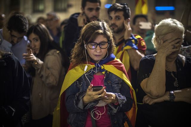 스페인 정부의 자치권 박탈 결정에 반발해 거리로 나온 시민들이 21일 바르셀로나에 있는 카탈루냐 주청사 인근에 모여 휴대폰을 통해 푸지데몬 자치정부 수반의 연설을 듣고 있다. 바르셀로나=AP 연합뉴스