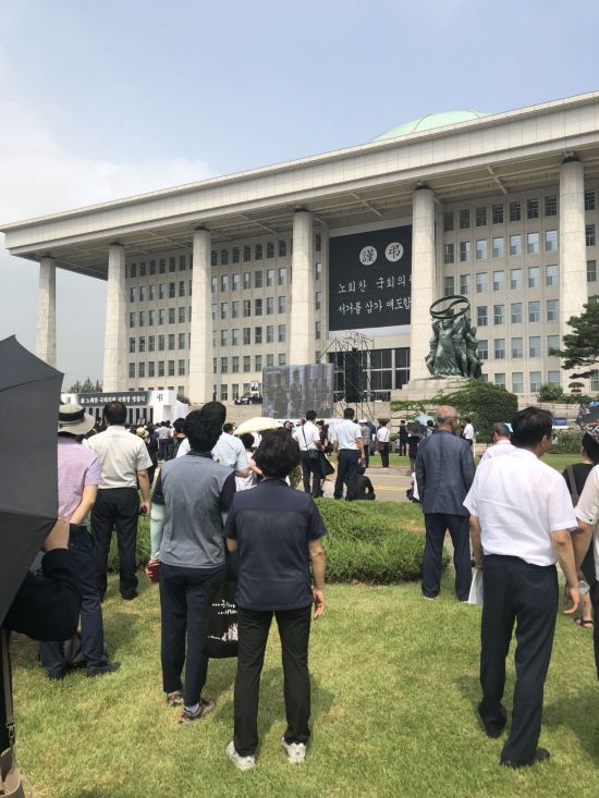 27일 국회 정현관에서 열린 故 노회찬 정의당 원내대표의 영결식장을 국회 청소노동자(가운데 뒷모습)가 지켜보고 있다.