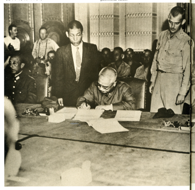 1945년 9월 9일 오후 4시 조선총독부 제1 회의실에서 ‘마지막 총독’ 아베 노부유키(가운데)가 남한 주둔 미군사령관 존 하지(오른쪽) 중장이 지켜보는 가운데 통치 이양 문서에 서명하고 있다. <한겨레> 자료 사진.