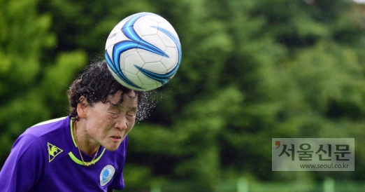많은 비가 내리고 있는 가운데 펼쳐진 경기에서 동작여성축구단 유정규(64) 선수가 헤딩을 하자 얼굴에서 땀과 빗물이 흩어지고 있다.
