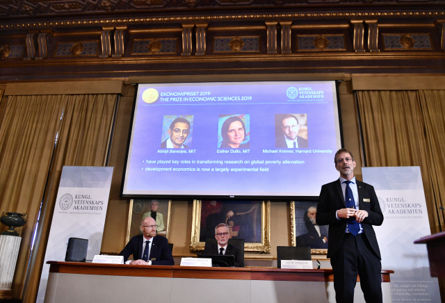 예란 한손(가운데) 스웨덴 왕립과학원 원장이 14일(현지시간) 스톡홀름에서 2019년도 노벨경제학상 수상자들을 발표하고 있다. 스크린에 수상자인 아브히지트 바네르지(왼쪽부터), 에스테르 뒤플로, 마이클 크레이머의 얼굴이 올라 있다. /AP연합뉴스