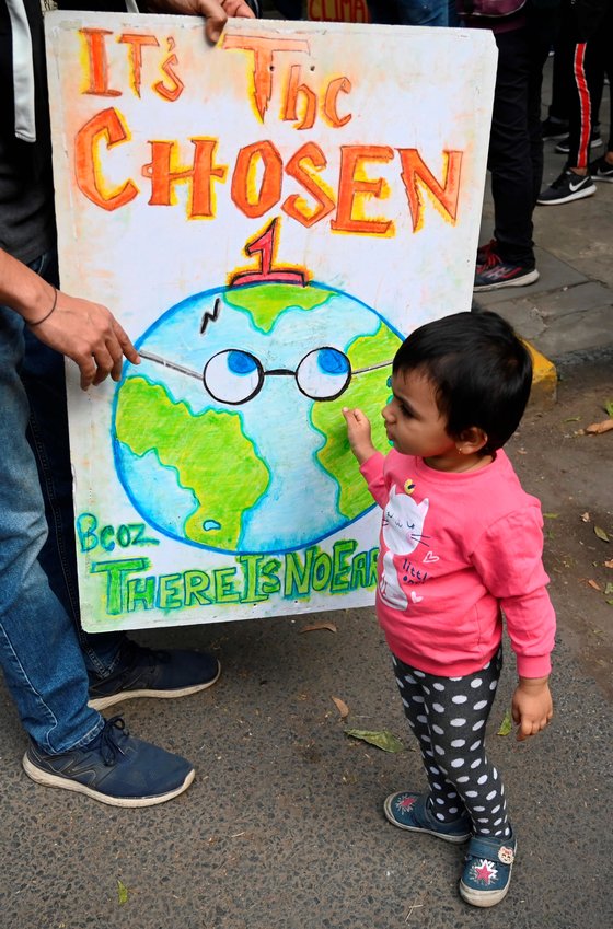 29일 인도 델리에서 한 어린이가 기후 변화에 대한 조치를 촉구하는 포스터를 보고 있다. [AFP=연합뉴스]
