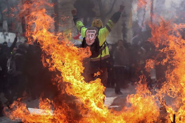 3월16일 프랑스 파리에서 한 시위자가 노란 조끼를 입고 '정신병자'라 쓰여진 마크롱 프랑스 대통령의 캐리커쳐를 등에 부착한 채 항의하고 있다. AFP 연합뉴스