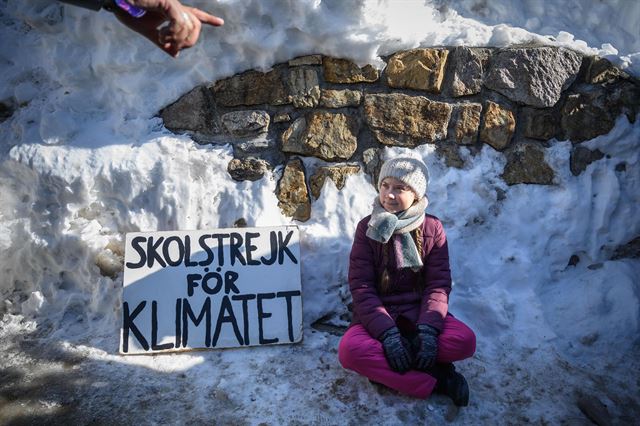 1월25일 스위스 다보스에서 세계경제포럼 회의가 열린 가운데 스웨덴의 어린 환경운동가 그레타 툰베리가 '기후변화를 위해 학교 파업' 이라 적힌 플래카드 옆에 앉아 시위를 하고 있다. AFP 연합뉴스