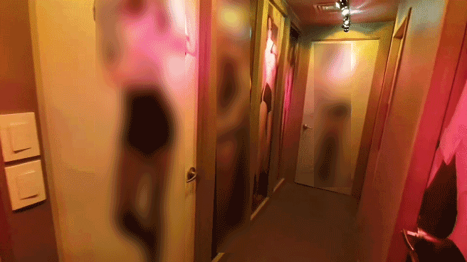 리얼돌 체험방에 들어서자마자 보이는 복도. 붉은 조명이 켜진 복도사이로 양옆에 약 8개 방들이 있다. 각 방문엔 각기 다른 리얼돌 사진이 붙어있다.