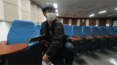 오른쪽 고정형 책걸상에서 힘겹게 노트필기를 하는 모습.