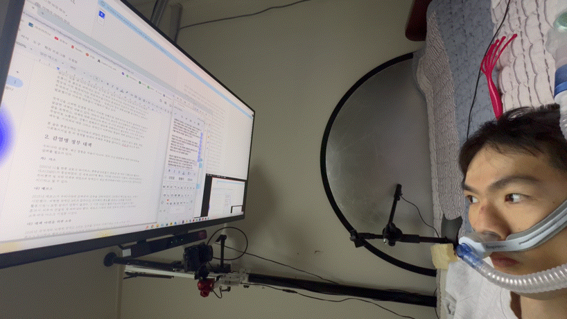 Jang Ik-seon types using his custom hybrid setup, mirroring his Galaxy smartphone onto his desktop to leverage predictive text — accelerating the process he uses to write with just his eyes. (Moon Joon-hyun/The Korea Herald)