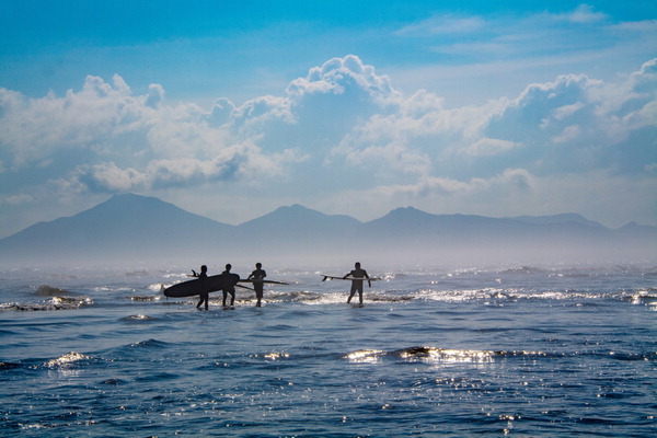 A scene of surfers walking along the beach with surfing boards at Dadaepo Beach