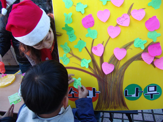 SK 자원봉사자와 함께 소망나무에 사진의 소망을 적어 꾸미는 아이